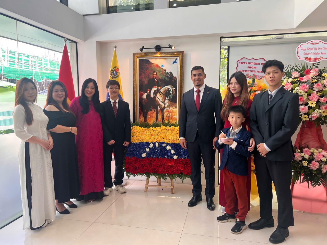 Đội ngũ JAI & TUT BRAND cùng Đại sứ Venezuela chụp hình trước không gian trưng bày quốc kỳ Venezuela và chân dung anh hùng giải phóng Simón Bolívar – biểu tượng cho khát vọng tự do và tri thức.